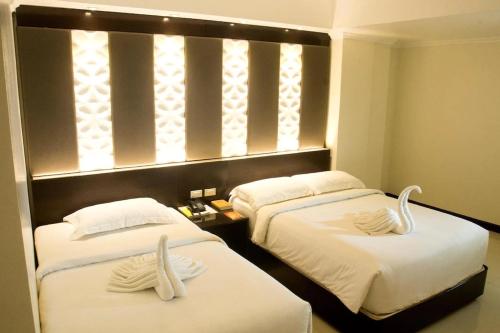 宿务M Citi Suites的两张床铺,位于酒店客房内,配有天鹅