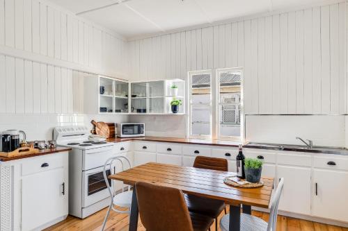 土乌巴Cheerful, Cosy Cottage - Near Rose Garden!的厨房配有白色橱柜和木桌