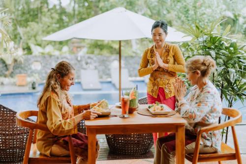 乌布Dewangga Ubud的三个女人坐在桌子上,一个女人站在