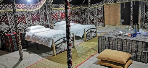 Ḩawīyah沙漠奇观营地酒店的帐篷内带2张床和桌子的房间