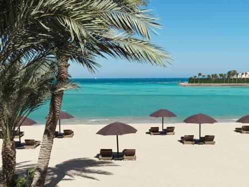 赫尔格达The Chedi El Gouna的海滩上设有椅子和遮阳伞,还有大海