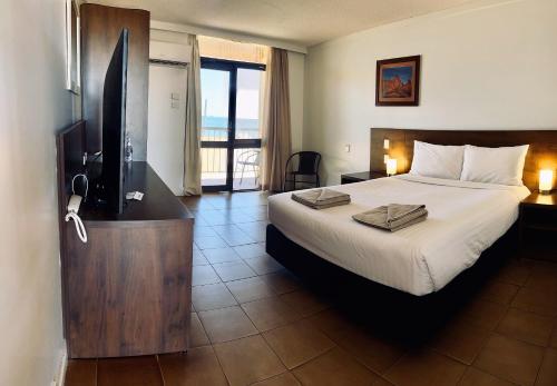黑德兰港Hedland Hotel的一间卧室配有一张床、一台电视和一个阳台