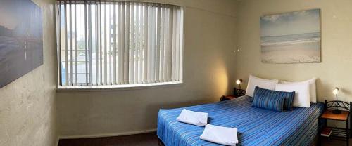 麦夸里港水景公寓的一间卧室配有一张带蓝色床单的床和一扇窗户。