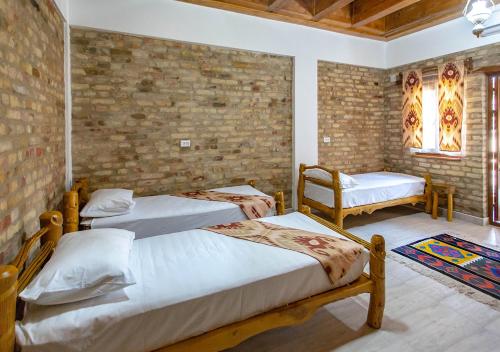 布哈拉Dervish Hostel的一间卧室设有两张床和砖墙