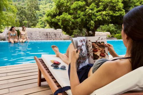 塔拉波托Pumarinri Amazon Lodge的坐在椅子上读书的女人在游泳池旁