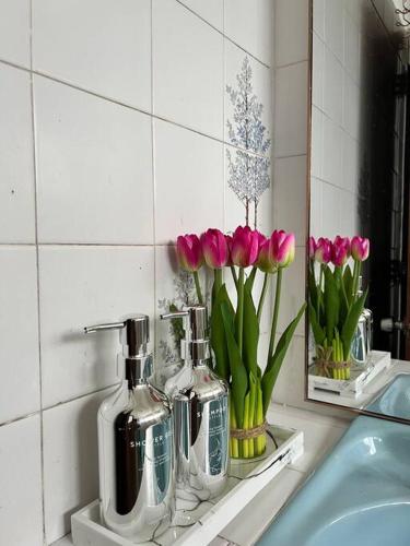 丹那拉打lily maison的浴室水槽,在架子上装有花瓶,上面装有粉红色郁金香