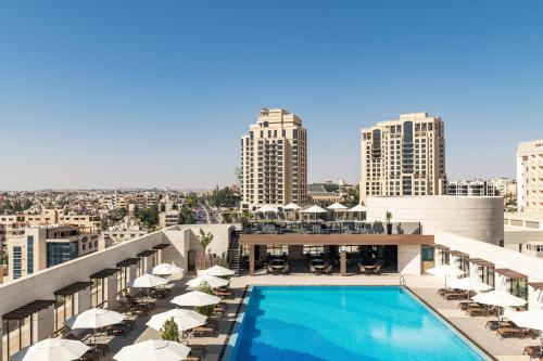 安曼Sheraton Amman Al Nabil Hotel的一座带椅子和遮阳伞的建筑屋顶游泳池