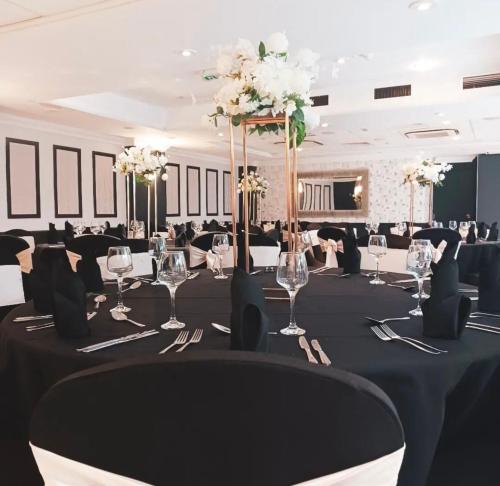 凯尼尔沃思Warwickshire Park Hotel的宴会厅,配有一张桌子,上面有黑色桌布和白色的鲜花