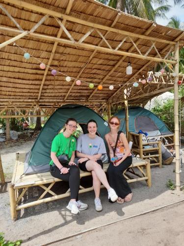 Ban NuaGanja Gardens Camping的三人坐在帐篷下的长凳上