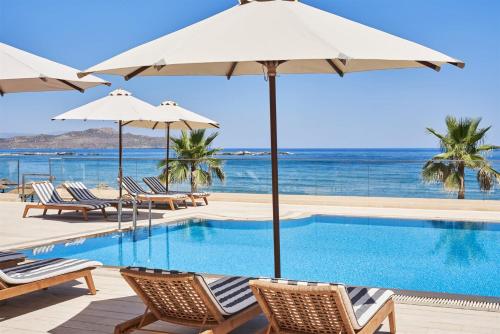 斯塔罗斯Atlantica Kalliston Resort - Adults Only的一个带椅子和遮阳伞的游泳池以及大海