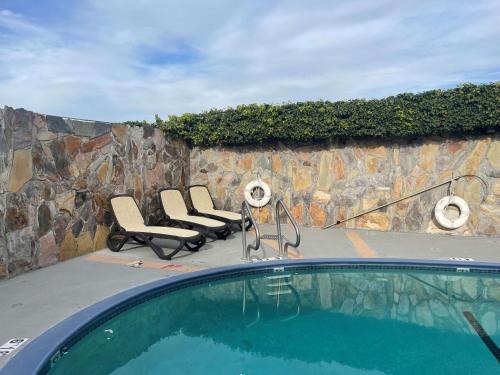 圣何塞SureStayPlus Hotel by Best Western San Jose Central City的一组椅子和一个游泳池,位于石墙旁