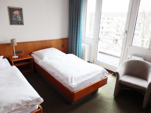 克雷费尔德曾特拉波斯图本酒店的一间卧室设有两张床、一把椅子和一个窗户。