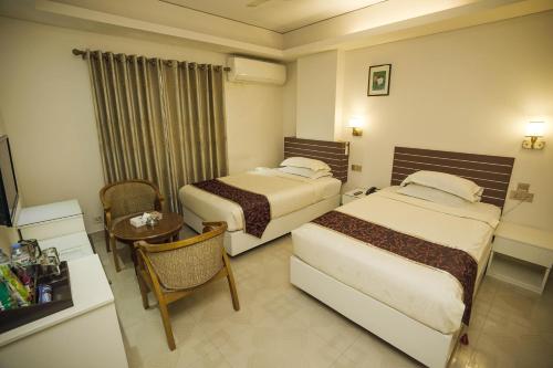 达卡Hotel Shuktara Dhaka的酒店客房设有两张床和一张桌子。