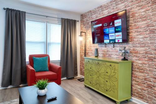 夏洛特Trendy Escape ◉ California King bed awaits!的一间客厅,客厅配有红色椅子和砖墙上的电视