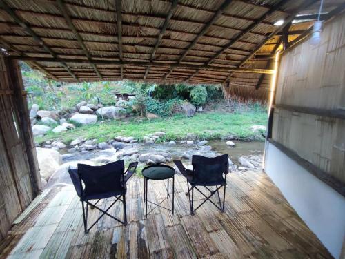 Ban Li KhaiForeste’ Camp的甲板上设有两把椅子和一张桌子,甲板上设有小溪