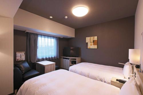 舞鹤市Hotel Route Inn Kyoto Maizuru -Nishi Maizuru Ekimae-的酒店客房设有两张床、一把椅子和电视。