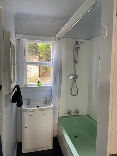 Baylys BeachToad Hall的浴室配有绿色浴缸、水槽和淋浴。