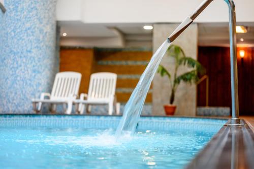 凯奇凯梅特Aranyhomok Business-City-Wellness Hotel的游泳池中的喷泉,带白色椅子