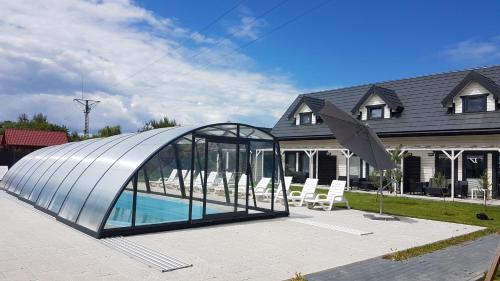 詹塔尔Osada Wypoczynku Jantar Resort&Spa - Luksusowe Domki z Basenem, Sauną i Jacuzzi的房屋前设有游泳池的玻璃凉亭
