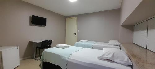 巴西利亚Pousada Kit Residence的客房设有两张床、一张桌子和一台电视。