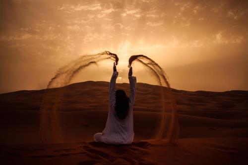 姆哈米德Mhamid Sahara Camp - Mhamid El Ghizlane的坐在沙漠中的女人,手放在空中