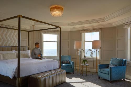 半月湾半月湾丽思卡尔顿酒店的一个人在卧室里,卧室里配有一张床和两把椅子