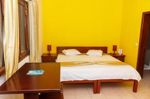 Cidade VelhaPousada Quinta Ribeirinha的一间卧室配有一张桌子和黄色墙壁的床