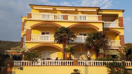 诺维·维诺多尔斯基Bed & Breakfast Ružica的黄色的建筑,设有白色的阳台,并种植了棕榈树
