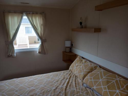 阿贝尔格莱D24 is a 2 bedroom 6 berth caravan close to the beach on Whitehouse Leisure Park in Towyn near Rhyl with decking and private parking space This is a pet free caravan的一间卧室设有一张床和一个窗口