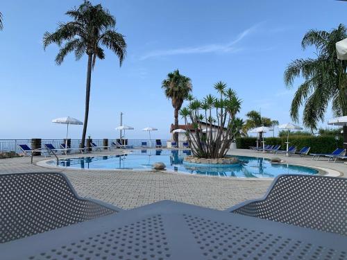 梵蒂冈角Rosy Hotel Residence的一个带椅子和棕榈树的游泳池以及大海