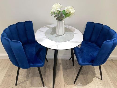 KentStylish Cosy Studio Apartment的一张桌子,上面有两把蓝色的椅子,花瓶