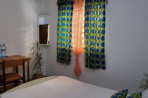 OuidahMaison fleurie Ouidah的一间卧室配有窗帘、桌子和床