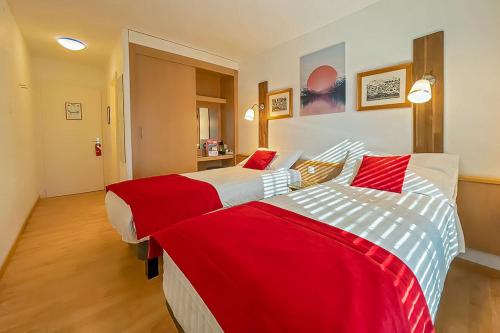 布勒Hotel des Alpes Bulle center的两张位于酒店客房的床,配有红色和白色床单
