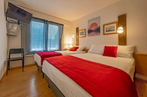 布勒Hotel des Alpes Bulle center的酒店客房,配有两张带红色床单的床