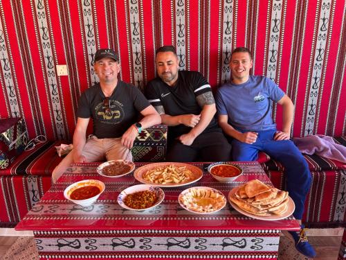 瓦迪拉姆Wadi Rum Mars Camp的一群三人坐在餐桌旁吃着食物