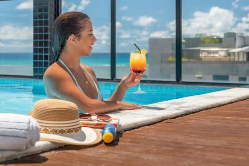 马塞约Palms Ponta Verde by Tropicalis的坐在游泳池旁喝一杯的女人