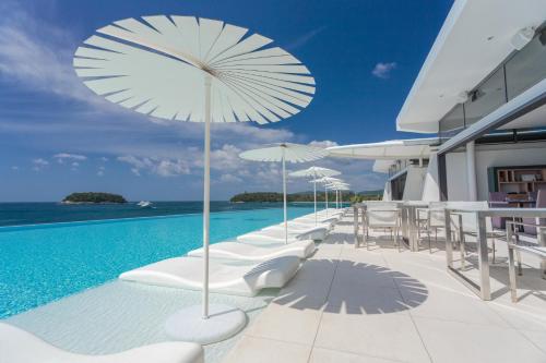 卡塔海滩Kata Rocks - SHA Extra Plus的一座大楼内带白色椅子和遮阳伞的游泳池