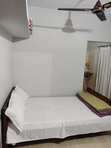 西里古里Newa Service Apartment的一间卧室配有一张带白色床单的床和风扇
