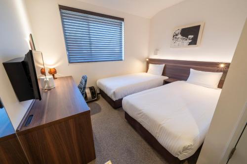 京都RESI STAY Jisco Hotel Kyoto Goshonishi的酒店客房设有两张床和电视。