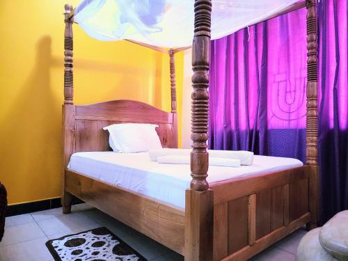 达累斯萨拉姆Jm Lodge - Kunduchi的一间卧室配有一张四柱床和紫色窗帘