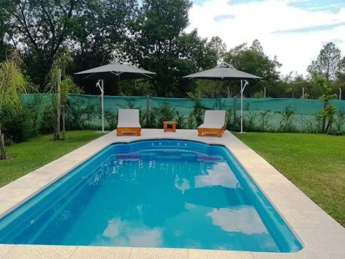 Villa Rosacasa con pileta climatizada, tiempo para descansar, Pilar的一个带两把椅子和两把遮阳伞的游泳池