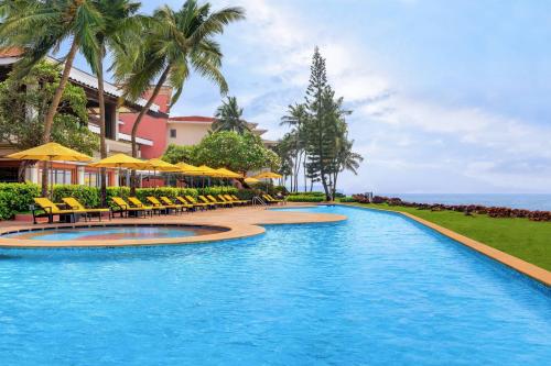 帕纳吉果阿万豪Spa度假酒店的度假村的游泳池,配有椅子和遮阳伞