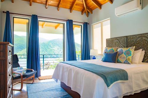 Jost Van DykeJost Van Dyke, BVI 3 Bedroom Villa with Caribbean Views & Pool的一间卧室配有一张蓝色窗帘的床和一个阳台
