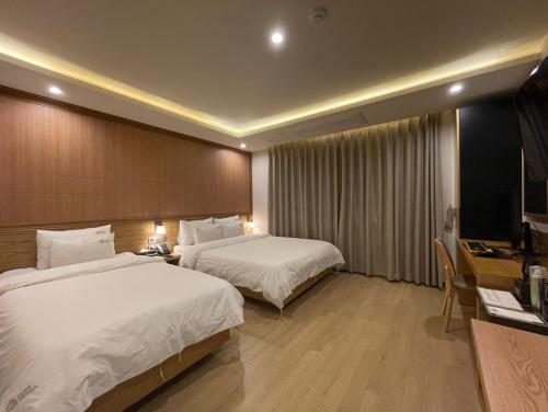 釜山Hotel Prima Busan的酒店客房设有两张床、一张桌子和一台电视。