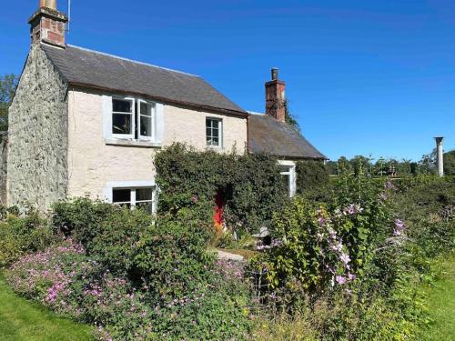 阿利士Charming, rustic & well equipped garden cottage的一座古老的石头房子,前面有鲜花