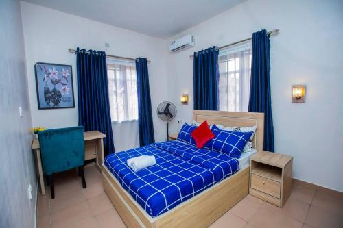 拉各斯AJI Warm 2BED Apartment (Ijegun, Lagos)的一间卧室配有蓝色的床、一张书桌和窗户。