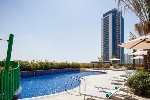 迪拜Holiday Inn & Suites - Dubai Science Park, an IHG Hotel的一座带椅子的游泳池,一座高高的建筑