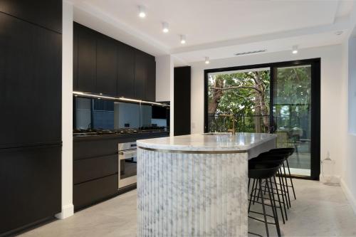 悉尼Luxury Waterside Home Sanctuary的一间厨房,配有黑色橱柜和一个带凳子的酒吧