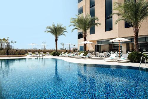 迪拜Holiday Inn & Suites - Dubai Science Park, an IHG Hotel的一座带椅子和棕榈树的游泳池,位于一座建筑前