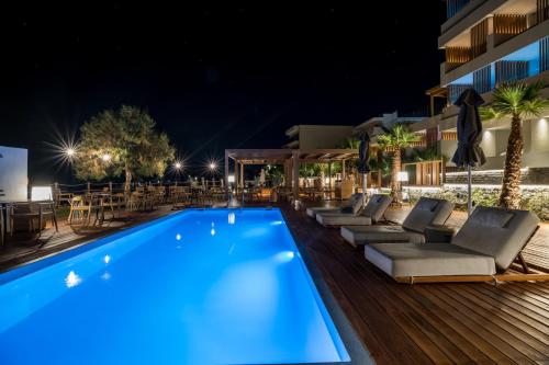 赫索尼索斯AKASHA Beach Hotel & Spa的夜间游泳池,配有躺椅和桌子